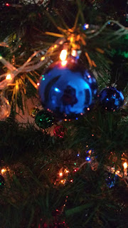 Árbol navideño con esfera navideña azul en primer plano y luces navideñas encendidas