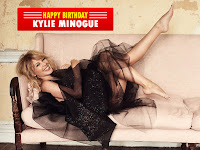 kylie minogue, lying on couch with bare feet and heart touching smile in black modern wear