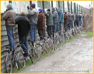 group-of-men-stands-on-bicycles-to-watch-over-fence-fun