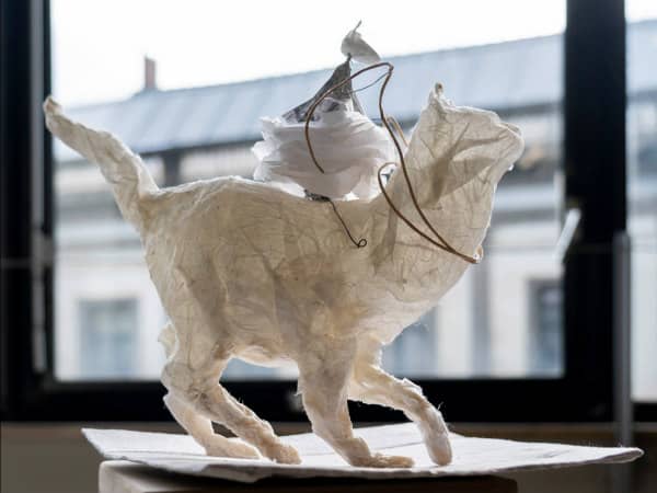 paper sculpture of white cat with mouse on its back, positioned on windowsill