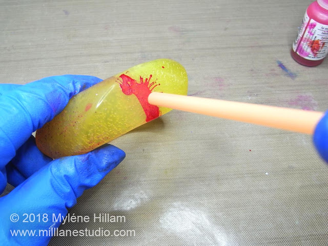 Bright pink alcohol ink being splattered onto a resin bangle by blowing through a drinking straw