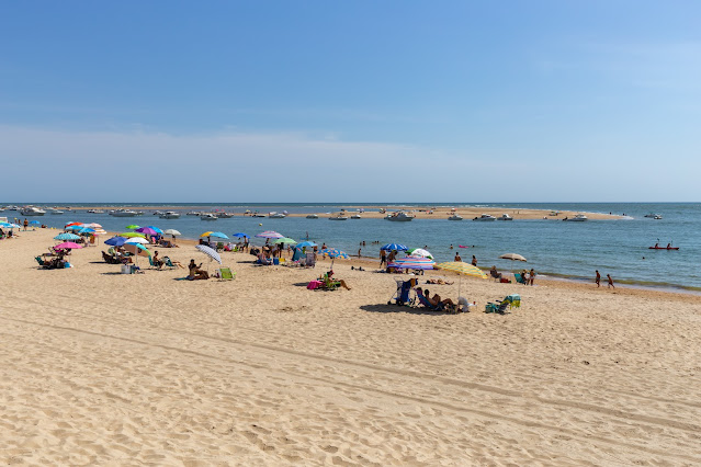 Playa de arena fina dorada con gente de vacaciones y las azules aguas del mar a su frente, un día soleado con cielo azul