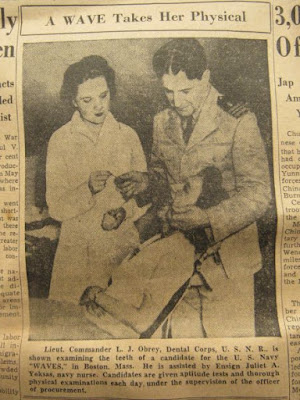 Black and white newspaper photo of woman in dental chair examined by nurse and man in Navy uniform. News caption reads: "Lieut. Commander L.J. Obrey, Dental Corps, U.S.N.R., is shown examining the teeth of a candidate for the U.S. Navy "WAVES," in Boston, Mass. He is assisted by Ensign Juliet A. Yoksas, navy nurse. Candidates are given aptitude tests and thorough physical examinations each day, under the supervision of the officer of procurement."