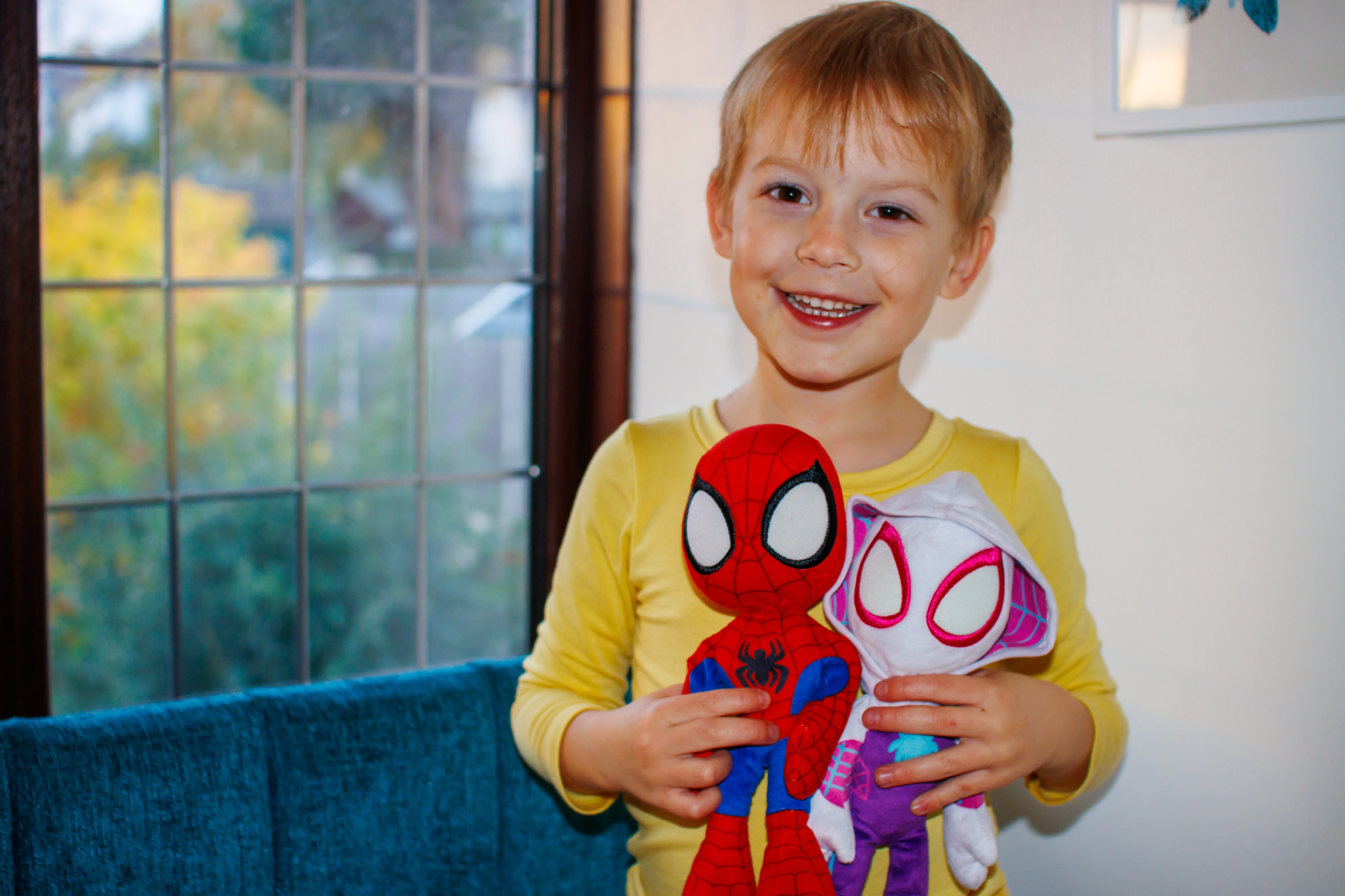 A young boy holding a spiderman and a ghost spider plush