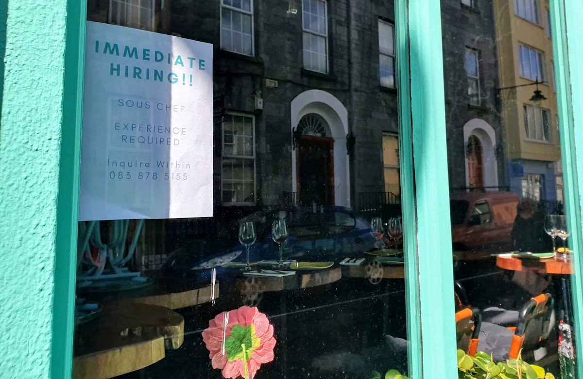 chef-wanted sign in a restaurant window, in Galway city, with a Georgian building reflected in it