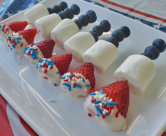 these are red white and blue fruits and marshmallows to celebrate a patriotic food party. Blueberries, strawberries dipped in white chocolate were used on a white plastic plate