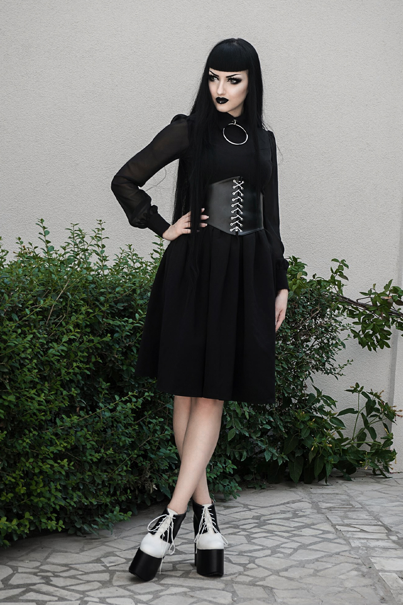 beautiful young woman in gothic black dress and a corset is posing for the camera on a street