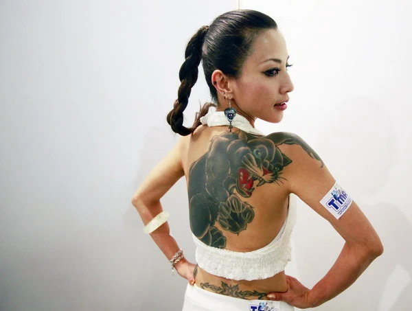 mujer asiatica posa de espaldas con vestido blanco, lleva tatuada en su espalda una pantera negra