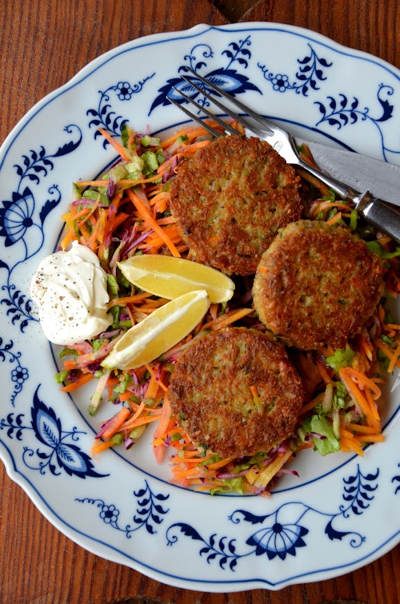 Drei knusprig goldbraun gebratene Grünkern-Laibchen liegen auf buntem Salat und sind mit Zitronenspalten garniert.