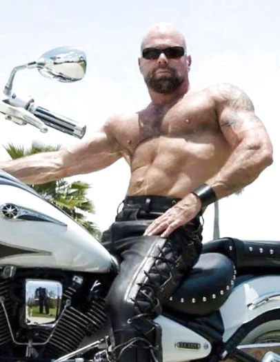 Bald sitting on a motorcycle shirtless and muscular with black leather pants on a sunglasses wearing man