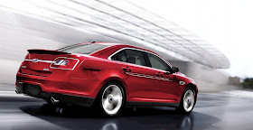 Rear 3/4 view of red 2011 Ford Taurus SHO driving around a building