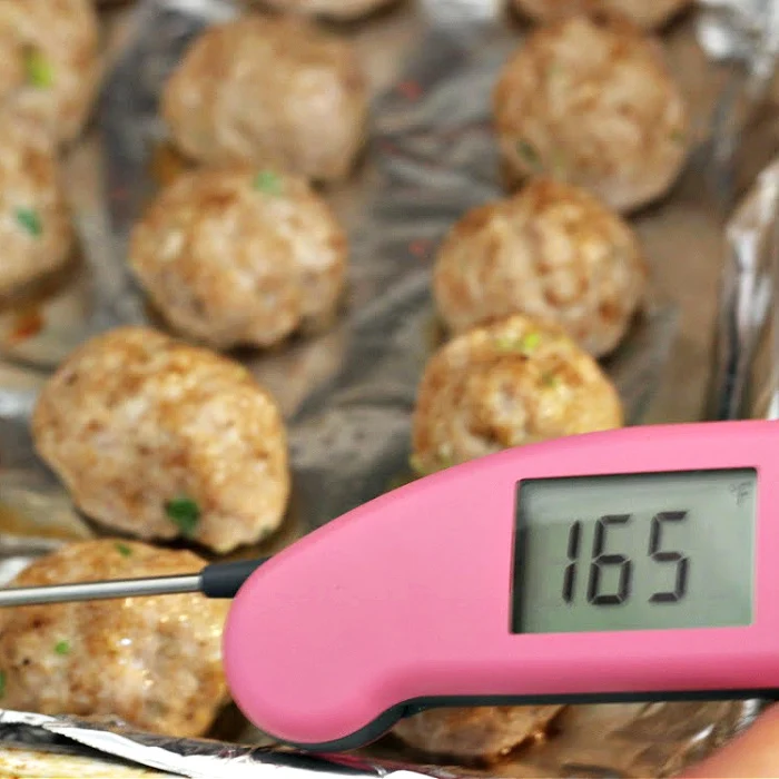 Asian pork meatballs out of the oven checking the internal temperature with an instant read meat thermometer reading 165 degrees F