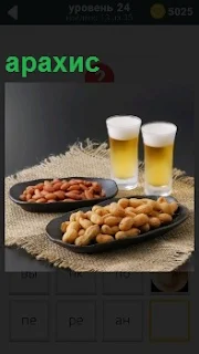 На столе стоят два бокала с пивом и в тарелках в качестве закуски орешки арахис