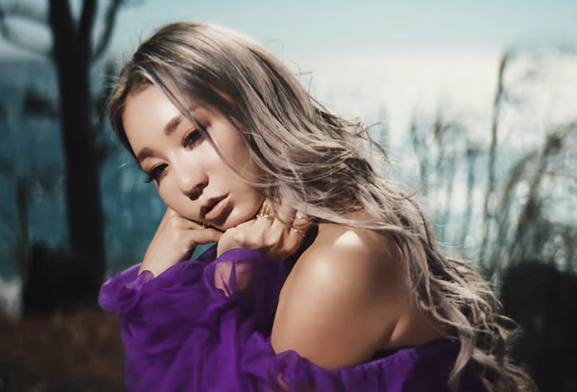 A screenshot of Koda Kumi in her music video for "Silence". Sat outside, wearing a purple dress made of (what looks like) silk and tulle.