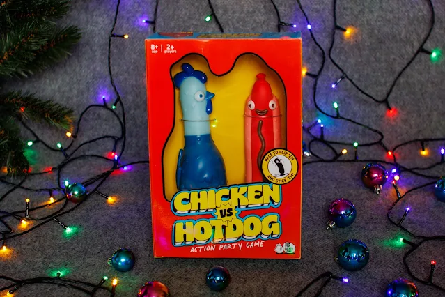 A red box with Chicken Vs Hotdog written on it and a blue rubber chicken and red hotdog visible