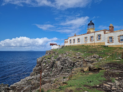 Low, white Lighthouse on a grassy cliff, blue sky and blue sea in bakcground.