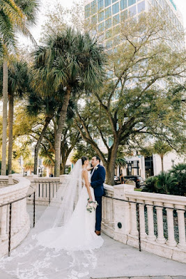 bride with long lace veil and groom kissing on walkway