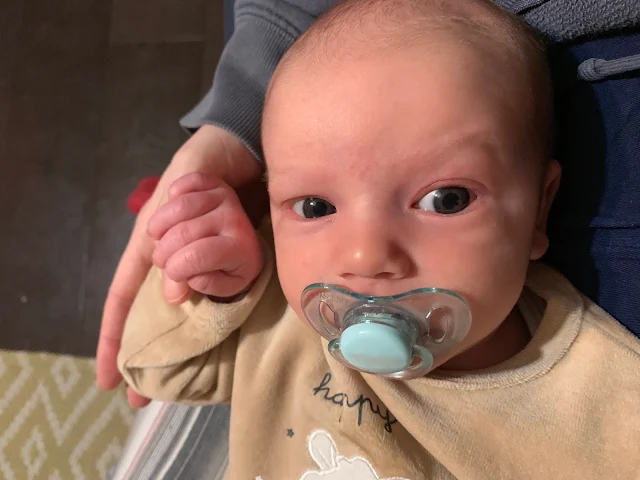 A baby holding on to mum's thumb and sucking on a dummy