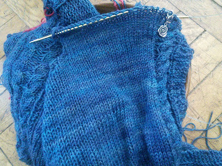 A dark blue sweater with the right front on a circular needle.  The other parts of the sweater are tucked in a yarn bowl under the right front.  The right front has been partially bound off for the armhole, and a single-twist cable runs along the other edge of the knitting. 