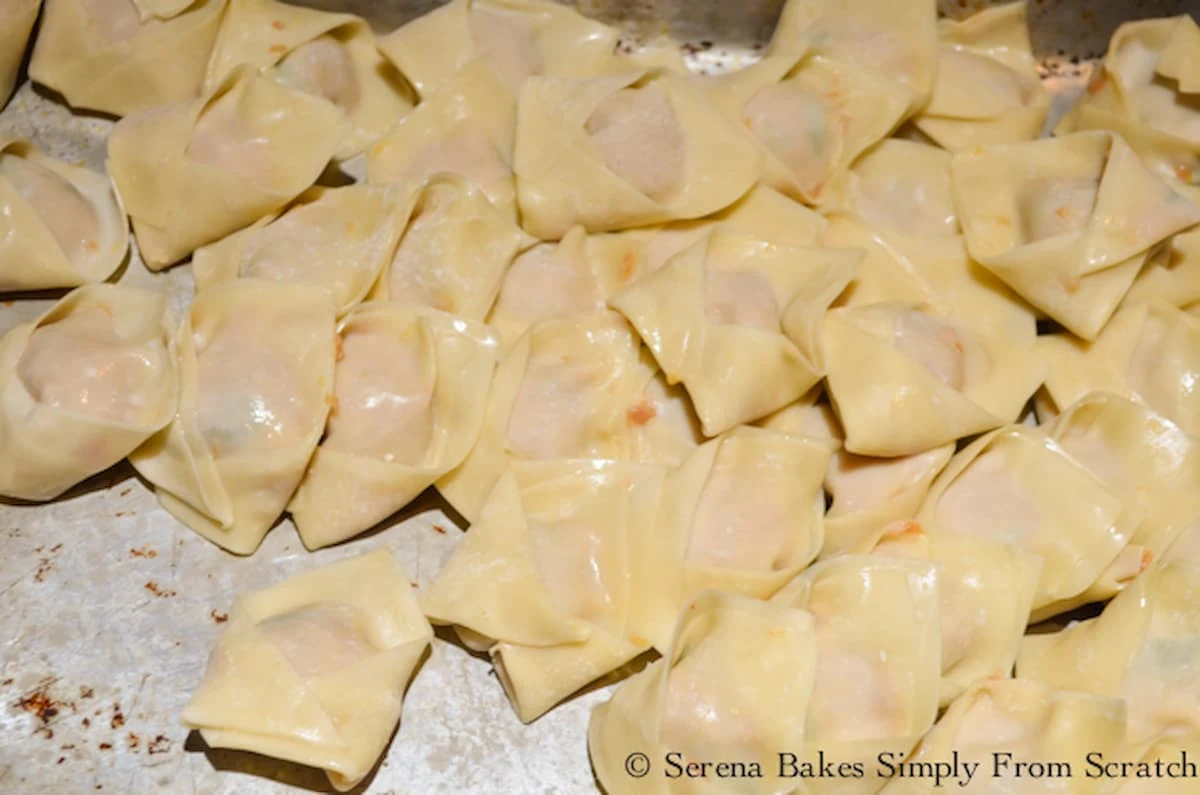 A larger pile of folded wontons on a cookie sheet.