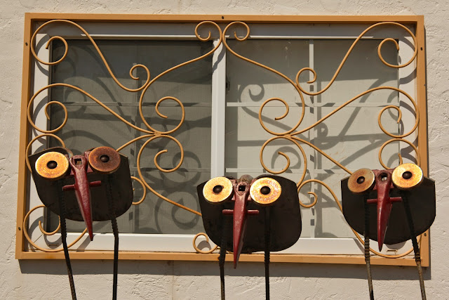 Three metal birds outside a window with a dated metal window cover at the Swetsville Zoo in Fort Collins, Colorado.