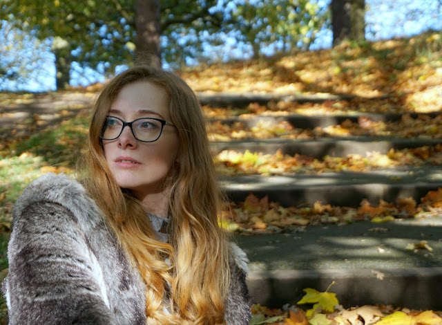 woman sitting outside in a park wearing a faux fur coat and looking off camera