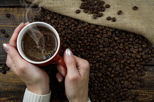Manos de mujer sosteniendo una taza de café con granos de café sobre la mesa
