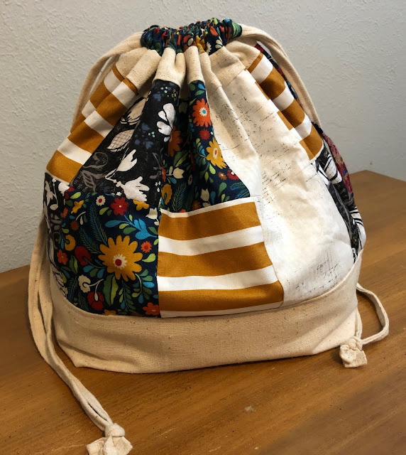 Finch bucket bag closed and standing up on a hope chest. There are floral prints and stripes.