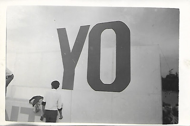A fotografia em preto e branco mostra um grande muro no qual há pintada a palavra “YO”, “EU” em tradução para o portugues. A frente do muro há um garoto de costas para a câmera o que dá ao leitor uma maior noção de perspectiva acerca do tamanho da pintura no muro.