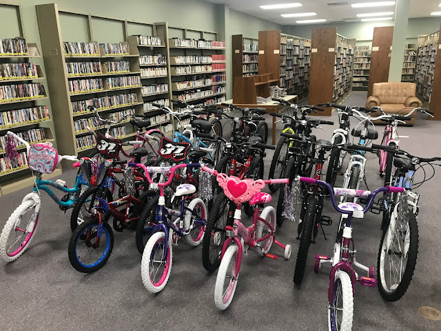 A collection of about twenty bicycles sits in the middle of a library.