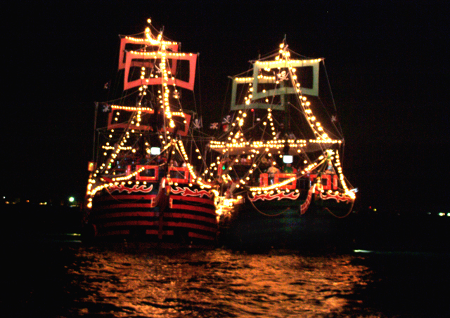 Two pirate ships at sea are decorated with lights in the midnight.