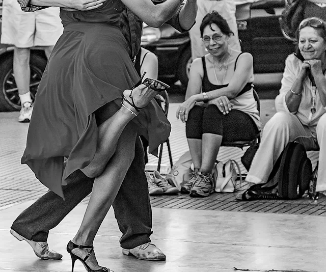 Gente sonriente mirando bailar tango.