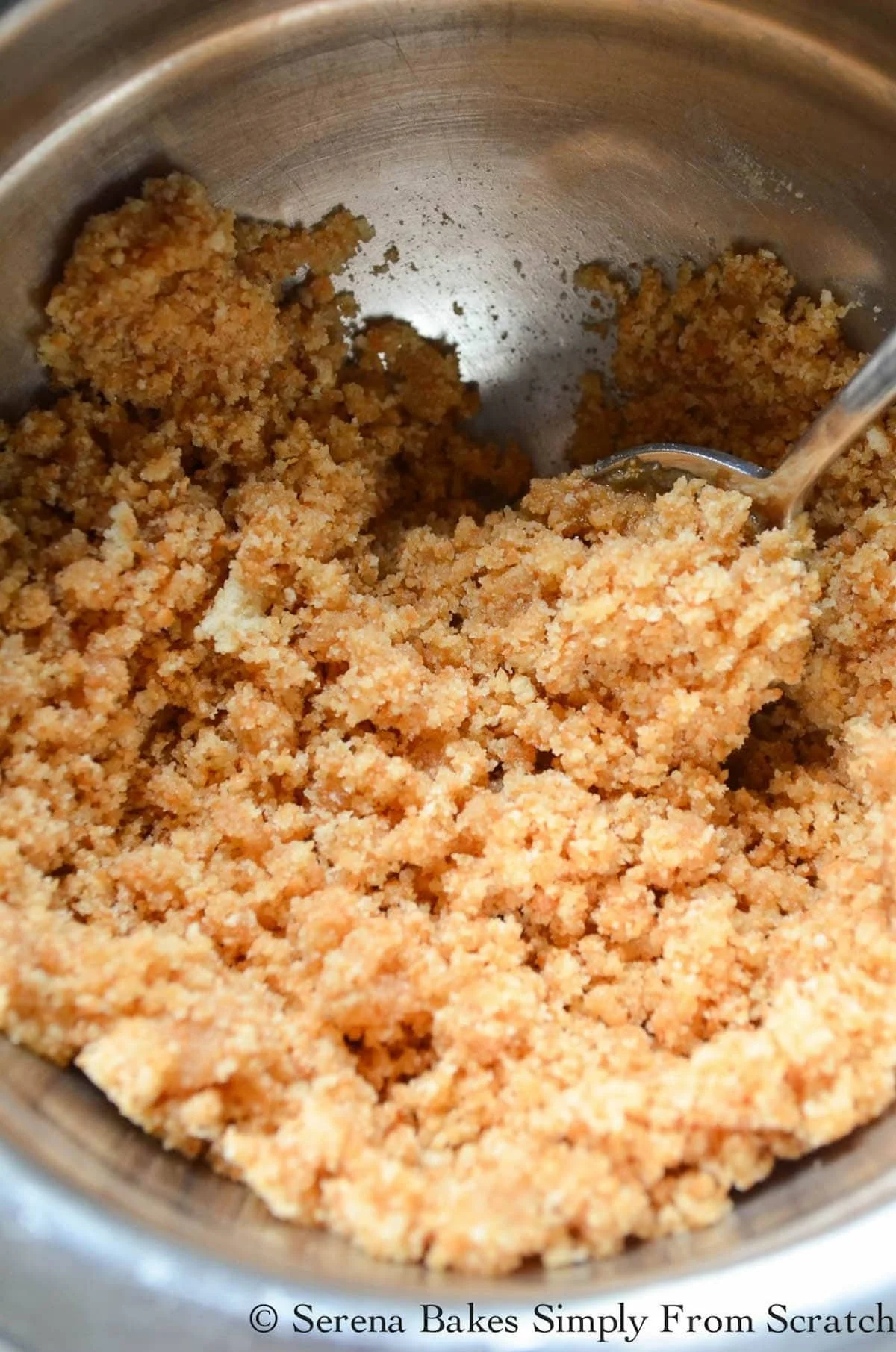 A sandy looking mixture of nilla wafer and sugar with butter in a stainless steel mixing bowl.