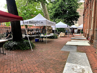 A row of farmers market tents with empty tables and pre-ordered bags stacked behind them.