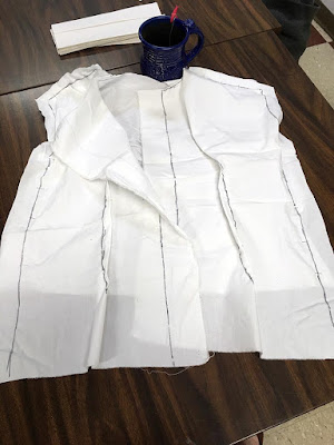 A white bodice muslin, looking pretty crumpled and shapeless, with black sharpie lines drawn along all the edges, laid out on a table with a blue tea mug just above it.