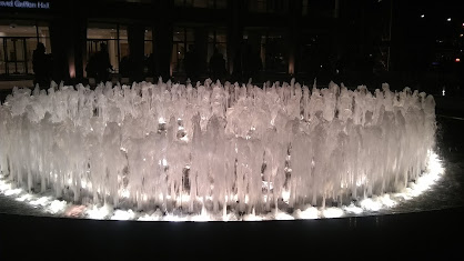 Photograph taken at night of the Lincoln Center fountain, lit up with fairly low jets of water in concentric rings.