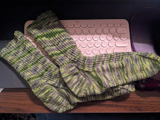 A pair of green and gray handknit socks sitting on a computer keyboard. THe lighting is bad but the socks make me happy.