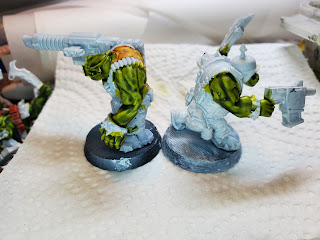 Two figures, back to back. The left one has brand name contrast paint on his back. Both of them have two colors of homemade green contrast paint on their skin.