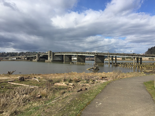 A bridge over water, with a cloudy sky above it. The bridge has a large concrete footing and an expansive bridge deck. The deck opens like a book from both sides for boats to travel under it.