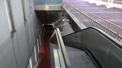 An escalator looking down into a tunnel entrance which has a red cycle track leading away.