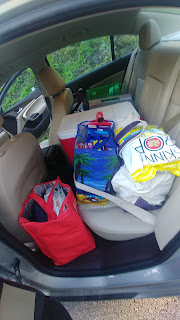A car back seat is full of bags, coolers, and food