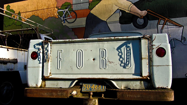 An old Ford pickup truck parked in front of a sweet mural in Portland Oregon with a California license plate that says 'Pacific Wonderland'.