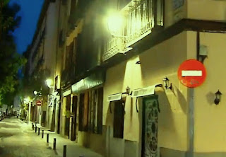 La pequeña calle con edificios de viviendas de cuatro o cinco plantas, iluminada por farolas adosados a sus fachadas.