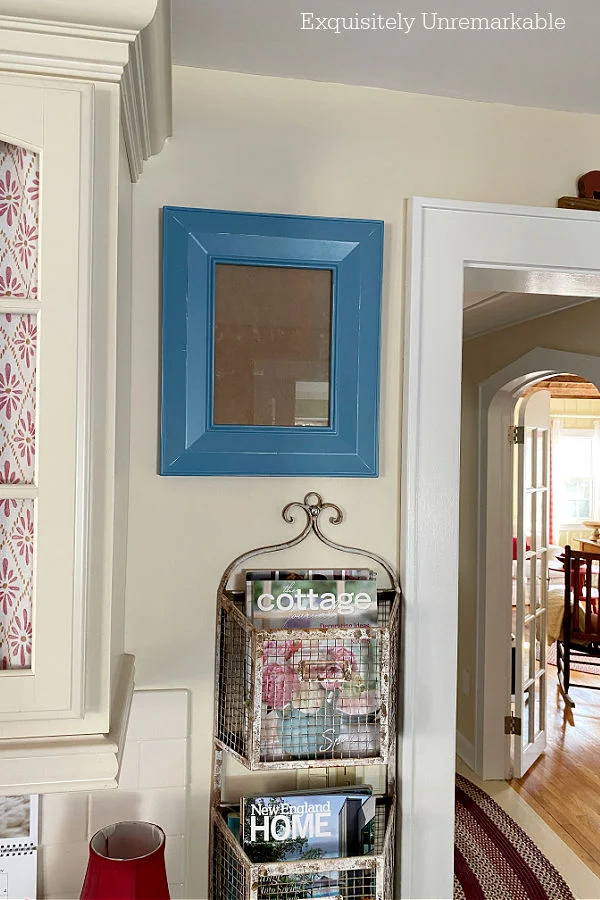 Blue wood picture frame hanging on the wall surrounded by red accents