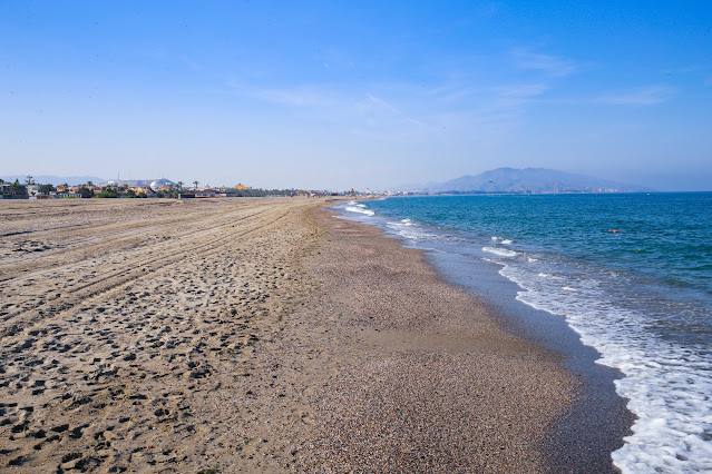 playa de arena llana y amplia con las azules aguas del mar a su frente
