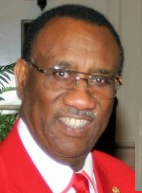 Photo of a middle-aged Black man with half-frame eyeglasses, wearing a red suit coat, red tie, and white shirt with red trim on the collar.