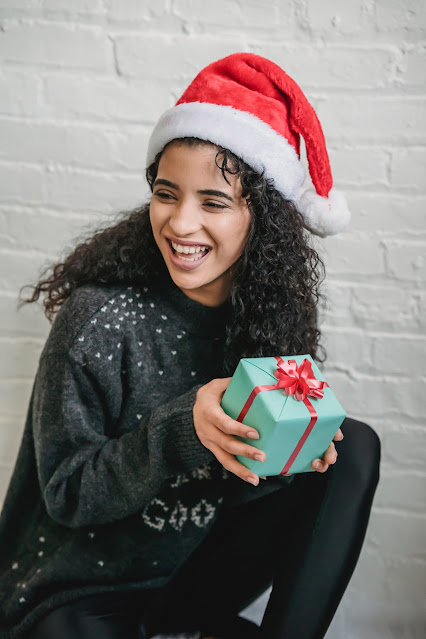 woman with curly hair wearing a Santa hat with gift in her hands.