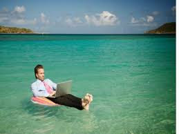 A shoeless man wearing a pink tie, with both legs stretched out and sitting on a floater in the middle of the sea while enjoying online education flexibility, on his grey laptop on his laps 