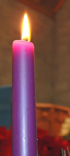 a tall, single purple candle burning brightly in the dark