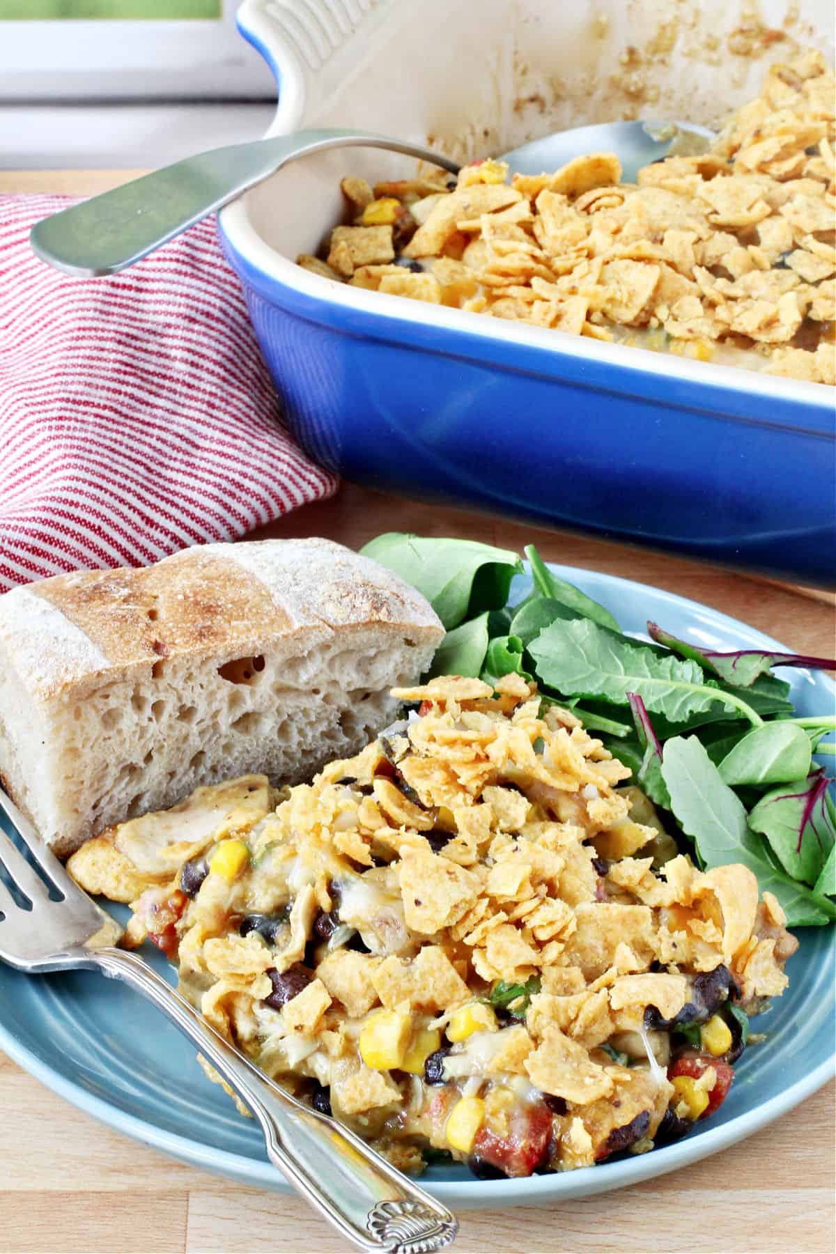 Slow Cooker Cheesy Chicken and Frito Casserole on a plate with a salad and bread.